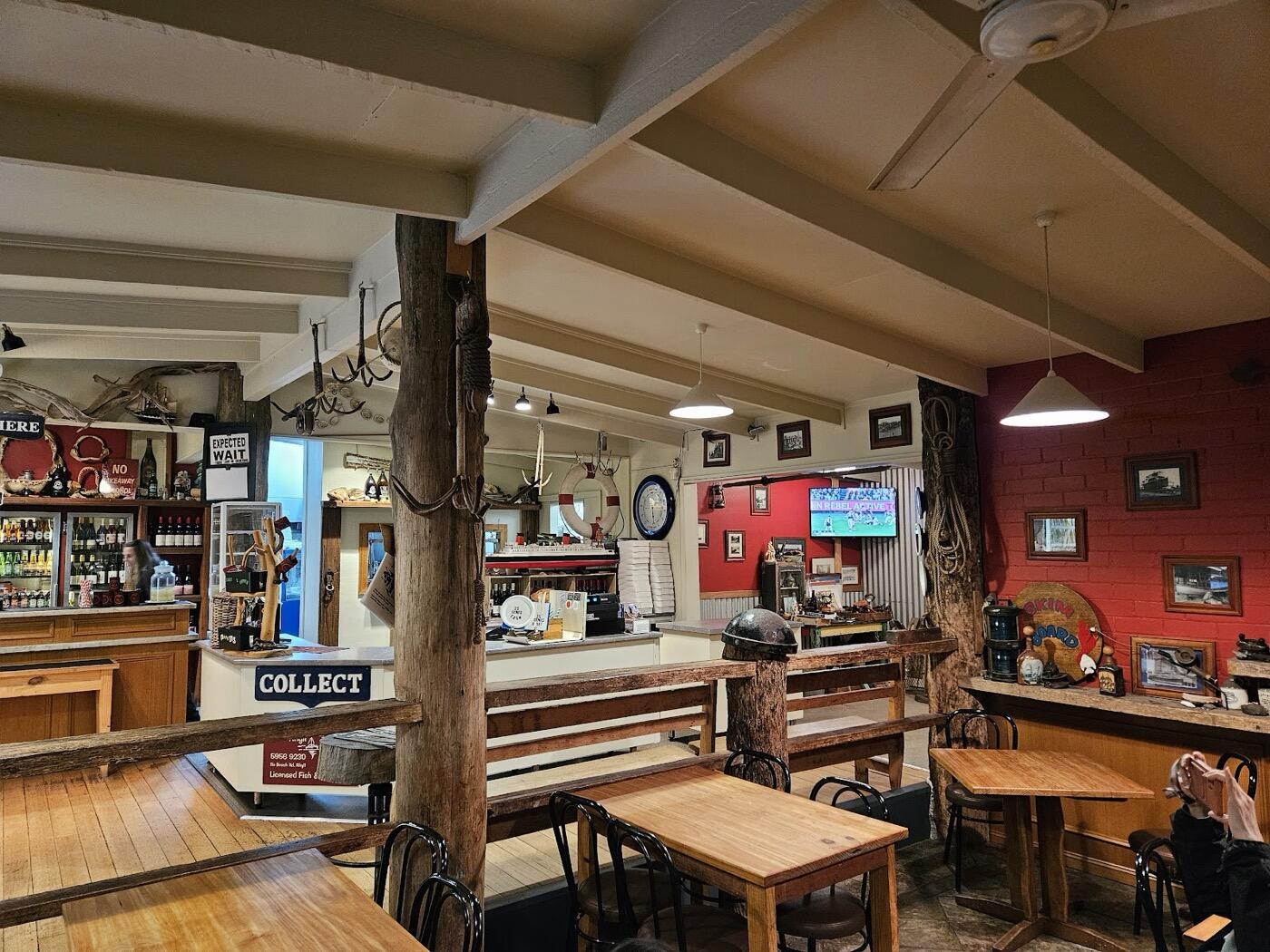 The dining room with timber tables, exposed ceiling beams, fishing memorabilia on the walls, a red feature wall and the counter in the background